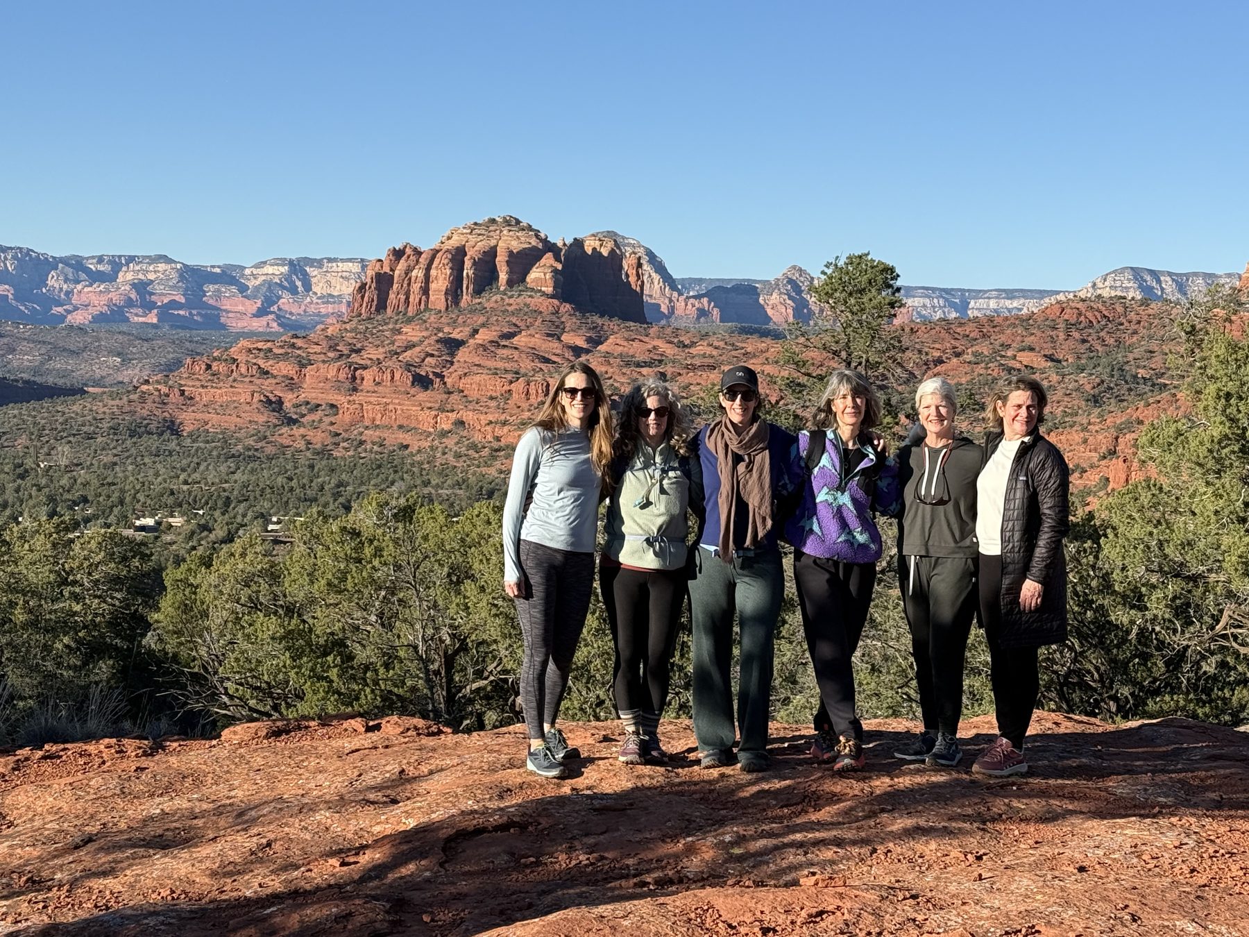 Six women standing together with red rock formations and the Sedona valley spread out behind them