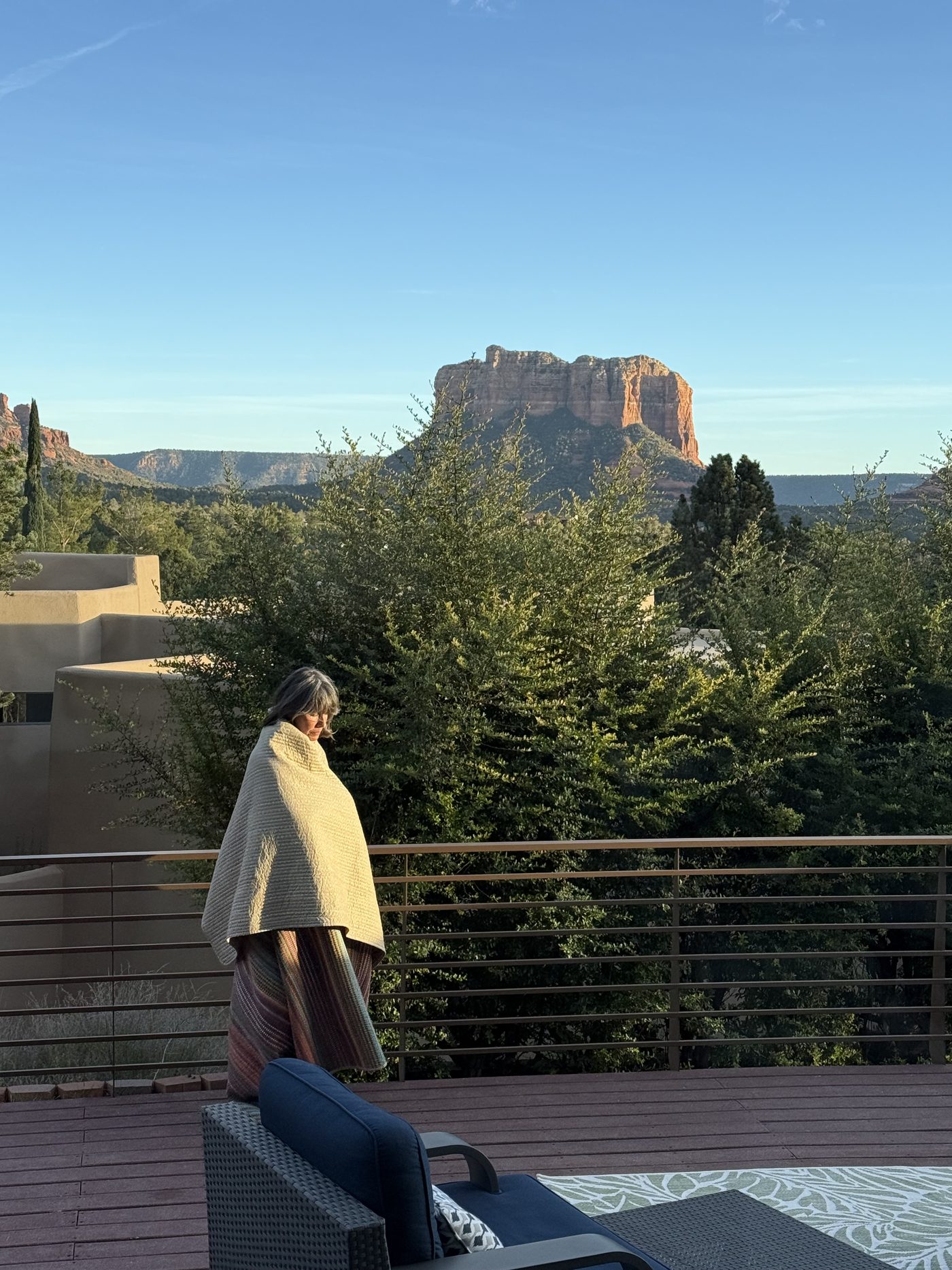 Ché standing wrapped in a blanket on a deck at dawn, red rock formations rising in the distance